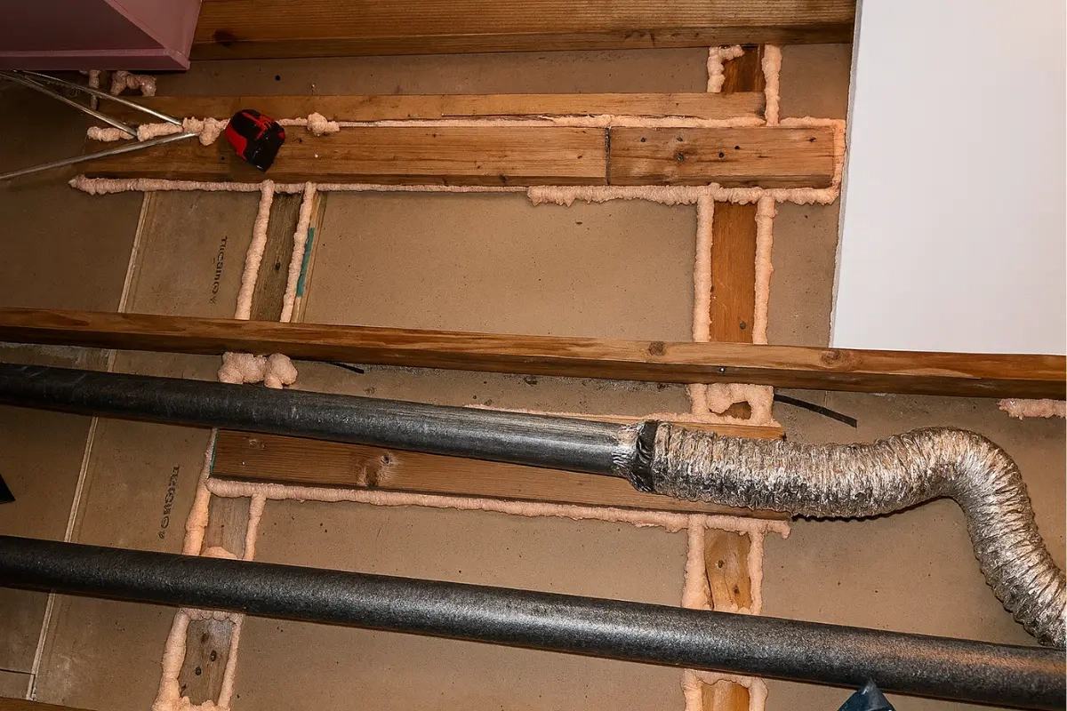 Alt Text Air sealing work inside an attic with spray foam applied around gaps and mechanical lines, shown as part of a home energy audit in Baltimore MD to identify and reduce heat loss.